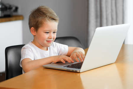 Funny young boy using a laptop computer sitting on top of a table at homeの写真素材