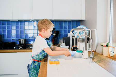 a little boy washes dishes in a modern kitchen