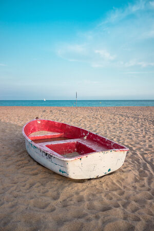 Old small white and red composite fishing boat on the beach and blue sky up the horizonの写真素材