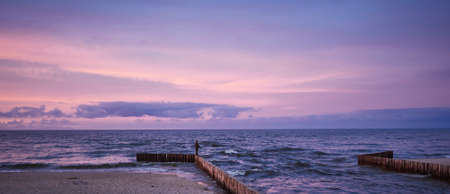 Man fishing in last rays of sunlight on sea breakwaterの写真素材