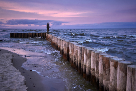 Man fishing in last rays of sunlight on sea breakwaterの写真素材