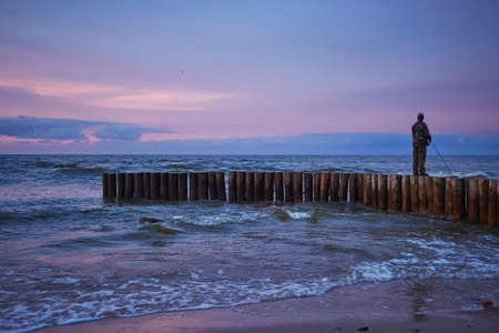 Man fishing in last rays of sunlight on sea breakwaterの写真素材