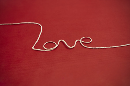 Love word made of white twine on red background for your Valentine or Momの写真素材