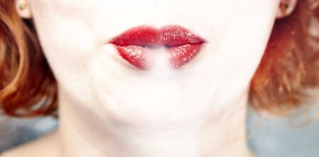 Young woman with red lips blowing out cigarette smoke.の写真素材