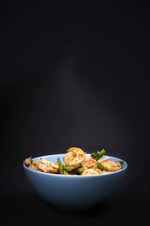 Hot fresh fried shrimps and asparagus served in a blue bowl on a black backgroundの写真素材