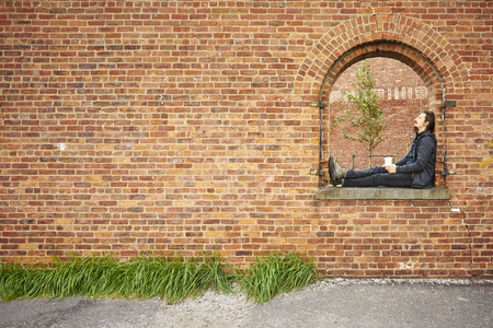 Young man rest on window of a red brick wall in the city.の写真素材
