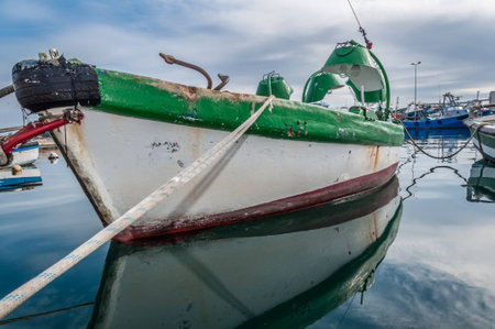 Reflections of fishing boat and a dramatic cloudy sky over water in the port of El Serrallo,...
