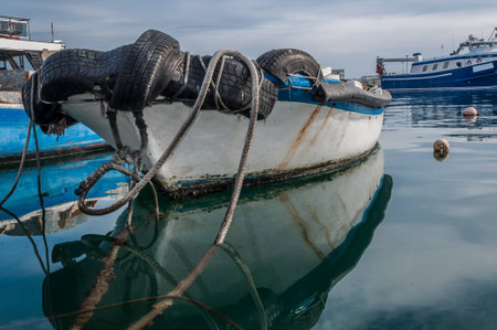 Reflections of fishing boat and a dramatic cloudy sky over water in the port of El Serrallo,...