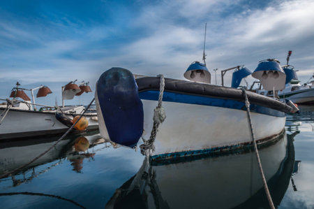 Reflections of fishing boat and a dramatic cloudy blue sky over water in the port of El Serrallo, Tarragona. spainの写真素材