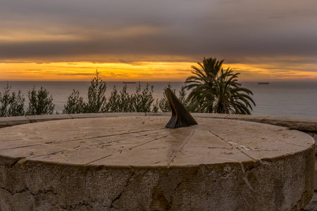 Orange color sunset with cloudy sky. A stone sundial is in front of the scene