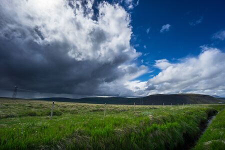 Iceland - River with green meadow and dark thunderstorm clouds coming as the sun shinesの写真素材