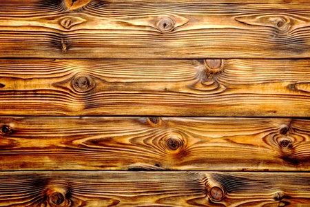 Detailed close-up of a warm-toned wooden surface with visible grain patterns and knots, ideal as a rustic background or texture.の写真素材