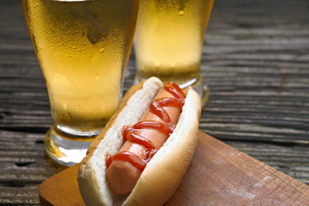 Hot dog with mustard and beer on wooden table, close-upの写真素材
