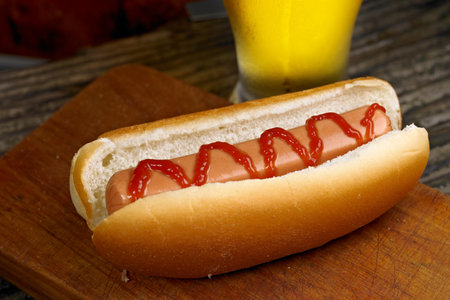Hot dog with ketchup and mustard on a wooden board with a glass of beerの写真素材