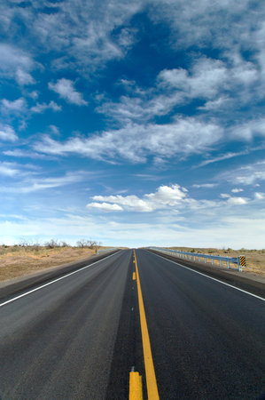 Asphalt road in the desert under blue sky with white clouds.の写真素材