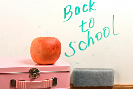 Back to school concept. Red apple on pink suitcase with blackboard