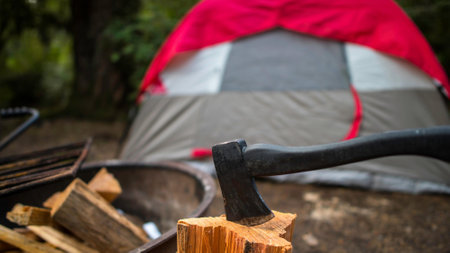 An ax stuck in a log with a tent in the background.の写真素材