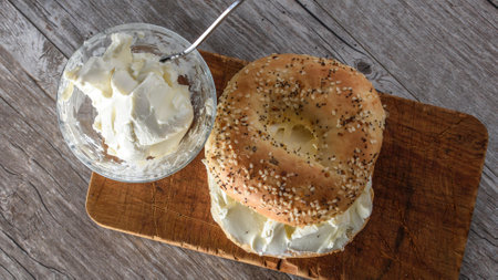 Bagel with cream cheese and sesame seeds on wooden boardの写真素材