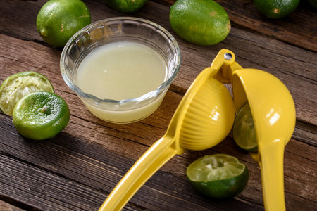 Fresh lime juice in a glass bowl with lemons on wooden backgroundの写真素材