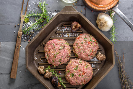 Raw hamburger patties in a pan with herbs and spices