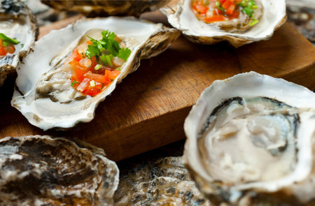 Fresh oysters with parsley and tomato on a wooden board.の写真素材