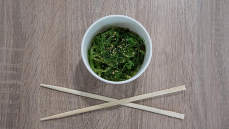 Green seaweed salad in a bowl with chopsticks on a wooden table