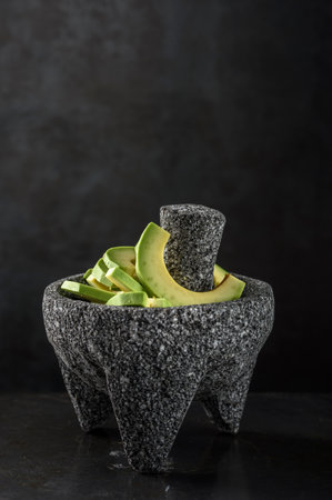 Mortar and pestle with avocado slices on a black background