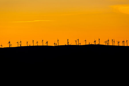 Silhouette of wind turbines at sunset on the hillside.の写真素材