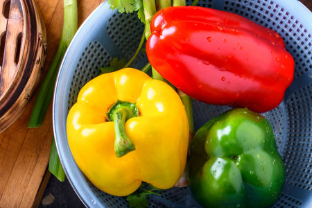 Red, yellow and green bell peppers in a colander on a wooden tableの写真素材