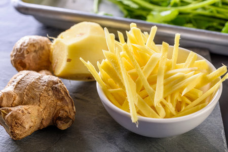 Ginger root and slices in a bowl on a slate background.