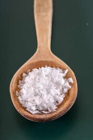Salt in a wooden spoon on a green background. Selective focus.