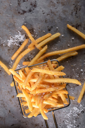 Golden French fries in a metal basket on a gray background, top view
