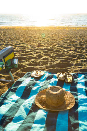 Straw hat, sun glasses and towel on the beach at sunriseの写真素材