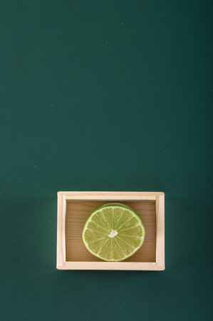 Fresh lime in a wooden box on a green background, top view