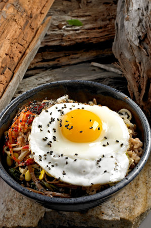 Bibimbap with fried egg in black bowl on wooden backgroundの写真素材