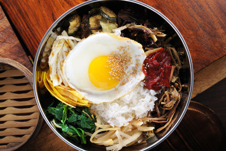 Bibimbap with rice, fried egg and vegetables on wooden backgroundの写真素材