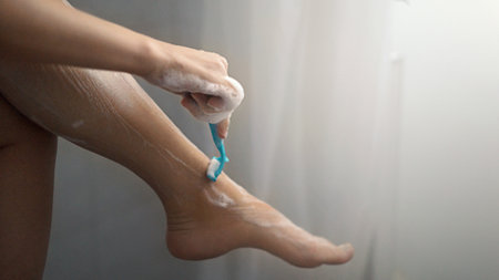 Woman shaving her legs with an electric razor, closeup of legs.の写真素材
