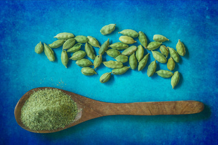 Cardamom powder in wooden spoon and cardamom pods on blue backgroundの写真素材