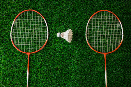 Badminton rackets and shuttlecock on green grass background.