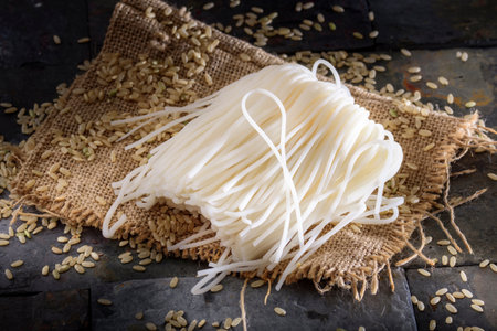 Raw rice noodles with sesame seeds on sackcloth and black background