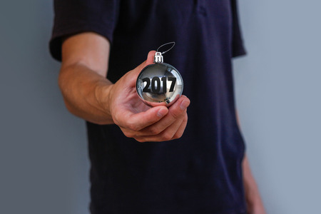 Man in black t-shirt holding Christmas toy ball silver with inscription 2017.の写真素材