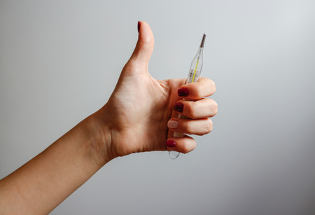 Female hand holding a mercury thermometer and shows thumb upの写真素材