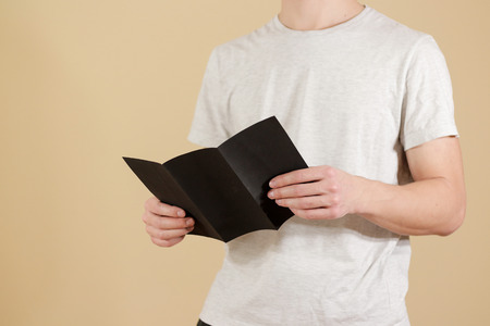 Man showing blank black flyer brochure. Read detailed booklet. Leaflet presentation. Pamphlet hold hands. Man show clear offset paper. Sheet template. Booklet design sheet display read first personの写真素材
