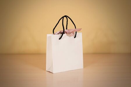 Blank white paper gift bag with a bow mock up standing on a wooden table. Empty plastic package mockup stand on table isolated. Consumer pack ready for logo design or identity presentation.の写真素材