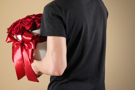 Man in black t shirt holding in hand rich gift bouquet of 21 red roses. Composition of flowers in a white hatbox. Tied with wide red ribbon and bow.の写真素材
