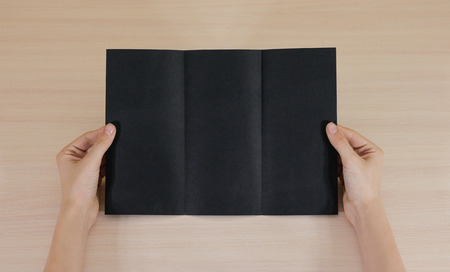 Hands holding blank black brochure booklet in the hand. Leaflet presentation. Pamphlet hand man. Show offset paper. Sheet template. Book in hands. Booklet folding design. Fold paper sheet display read.の写真素材