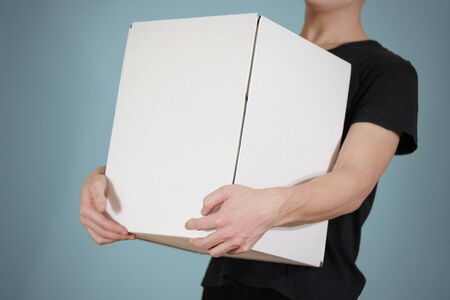 The guy in the black shirt holding a large white box. Carries a box on an isolated blue background.の写真素材