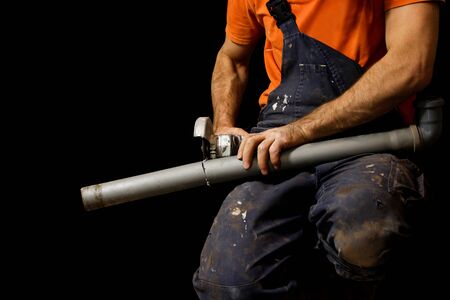 Man saws grinder plastic pipe. Isolated on black backgroundの写真素材