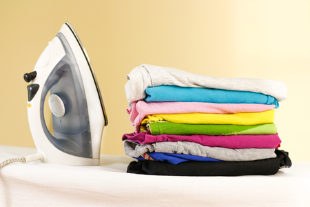 Iron stands with stacks of ironed colored linen. Pile of clothes. Ironing concept. All colors of the rainbowの写真素材