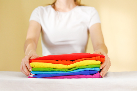 Girl hold on a stack of ironed colored linen. Pile of clothes. Ironing concept. All colors of the rainbowの写真素材